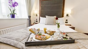 A hotel room with a neatly made bed, a tray of breakfast items, a vase with flowers, and a window with curtains.