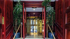 A hotel entrance with a red wooden door, glass doors, and a staircase with golden handrails.