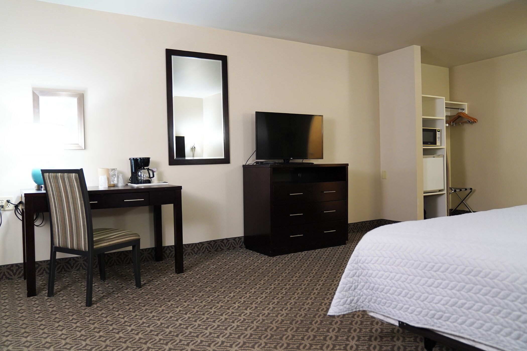 A hotel room with a bed, a desk, a chair, a television, a dresser, and a wardrobe.