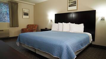 A hotel room with a large bed, a chair, a nightstand, a picture on the wall, and a window with curtains.