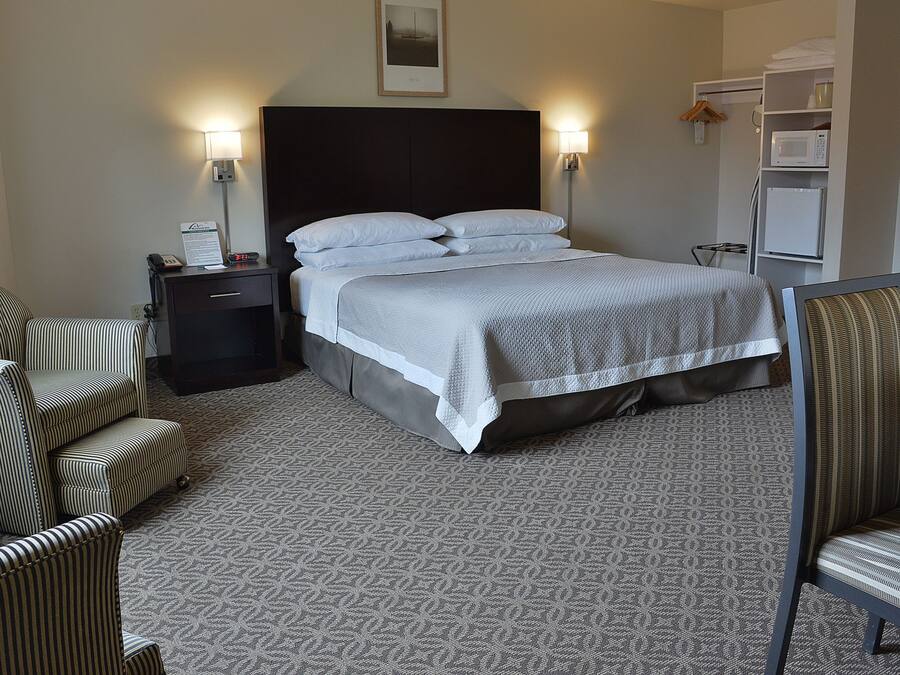 A hotel room with a bed, two bedside lamps, a nightstand, a chair, a wardrobe, and a microwave.