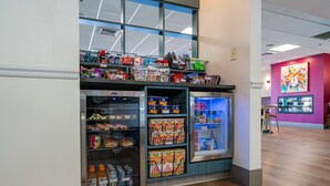 A vending machine area with snacks and drinks, a window with a view, and a pink wall with artwork.