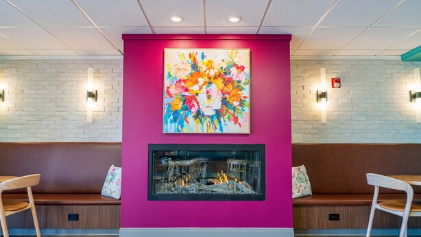 A reception area with a vibrant pink wall, a colorful abstract painting, a fireplace, and two wooden benches.