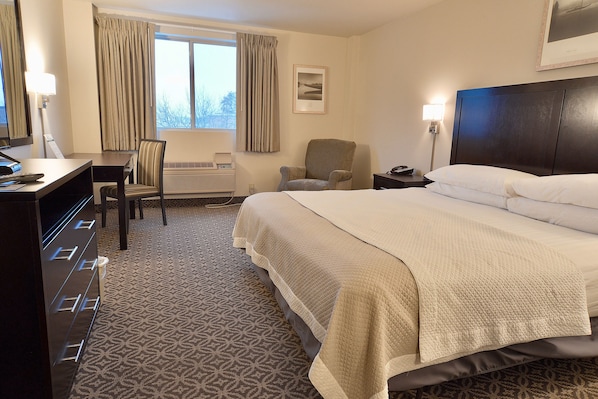 Une chambre d’hôtel avec un grand lit, un bureau avec une chaise, une petite table et une lampe.