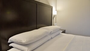 A neatly made bed with white linens and pillows, a dark headboard, and a bedside table with a lamp.