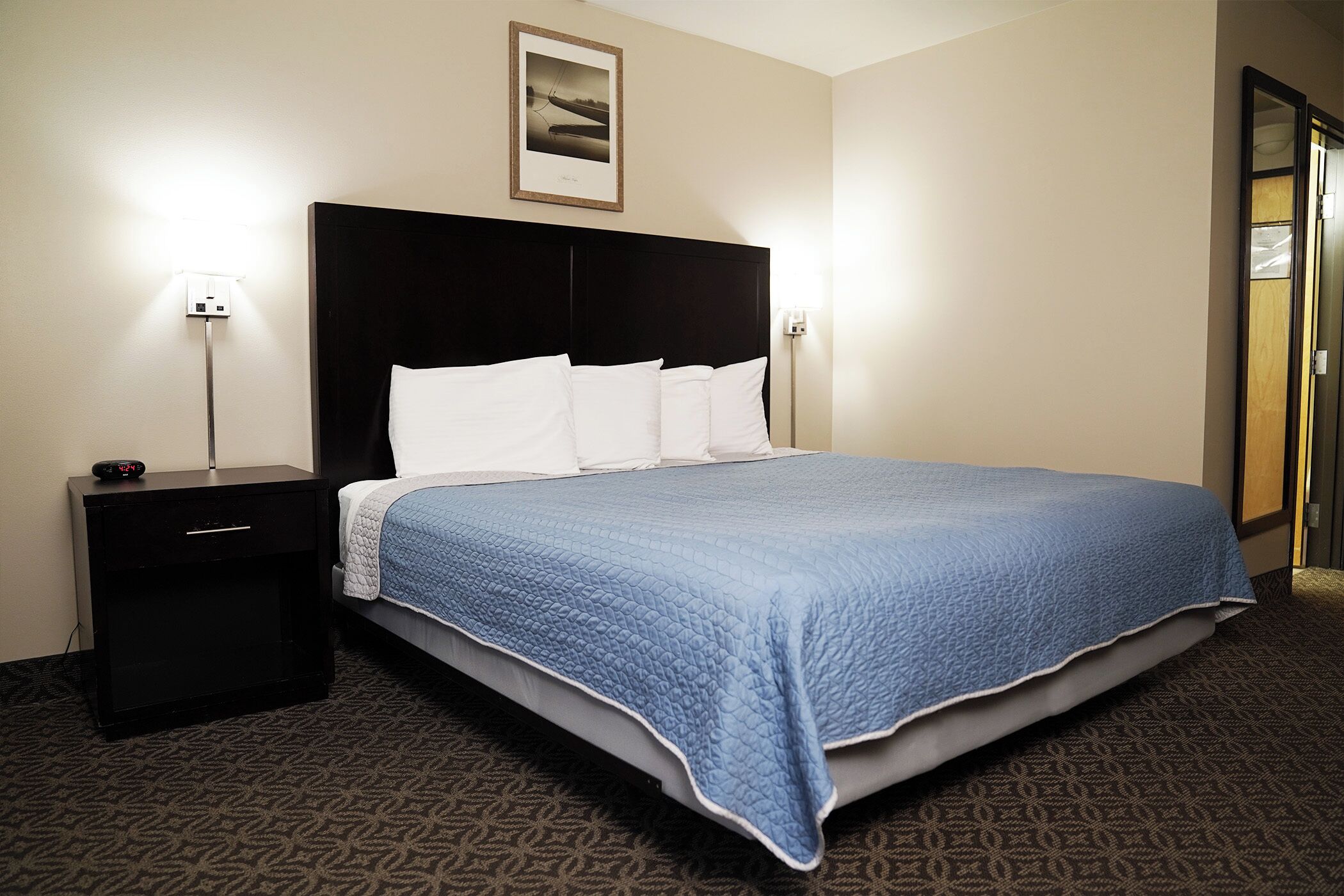 Una habitación de hotel con una cama grande, una mesita de noche, un cuadro en la pared y una puerta.