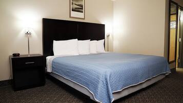 Una habitación de hotel con una cama grande, una mesita de noche, un cuadro en la pared y una puerta.