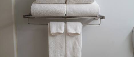 A bathroom with a towel rack holding two folded towels and two rolled-up towels.