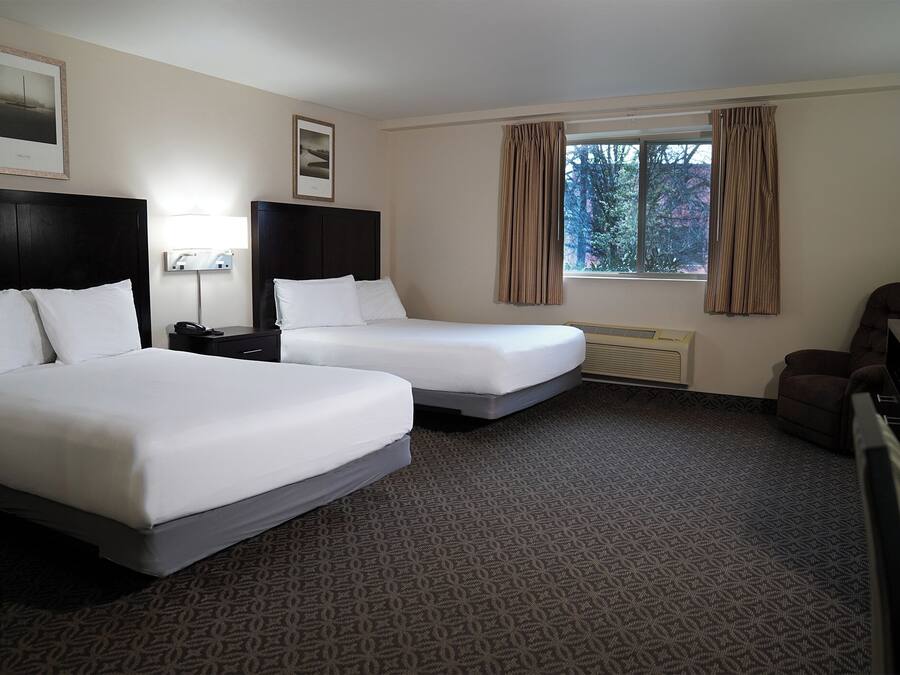 A hotel room with two beds, a desk, a chair, and a window with curtains.