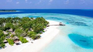 Una vista aerea di un resort tropicale con spiagge di sabbia bianca, acque cristalline turchesi e vegetazione lussureggiante.