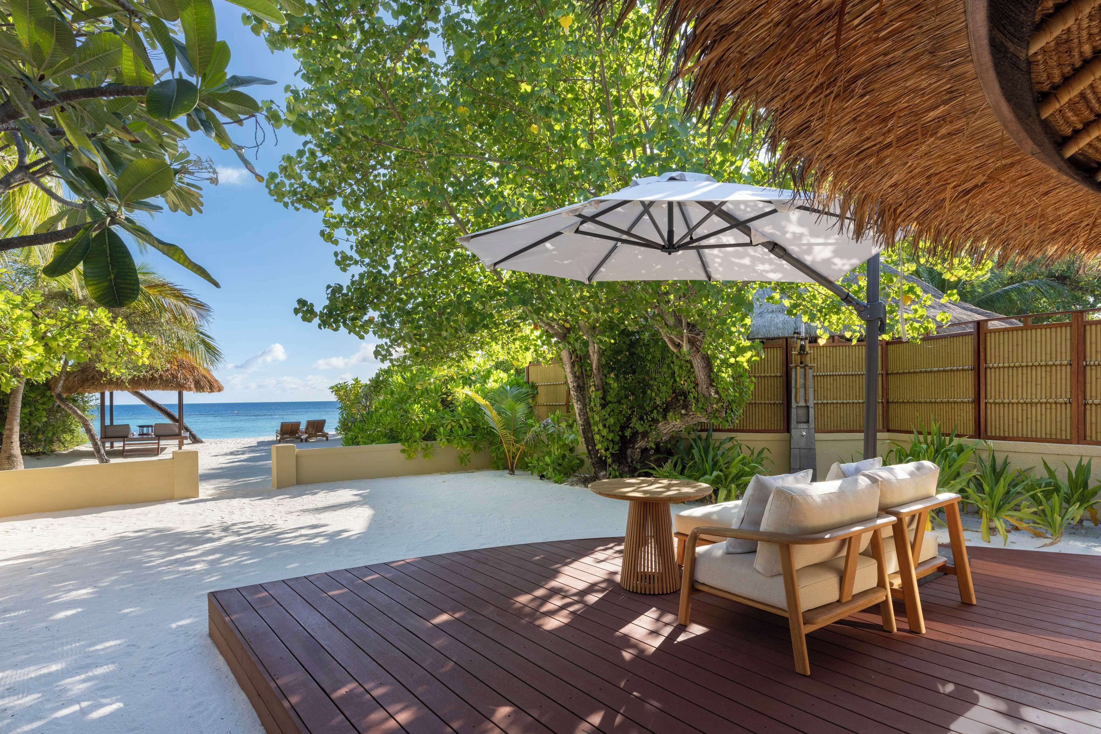 A wooden deck with a thatched umbrella, a wooden chair, and a small table.