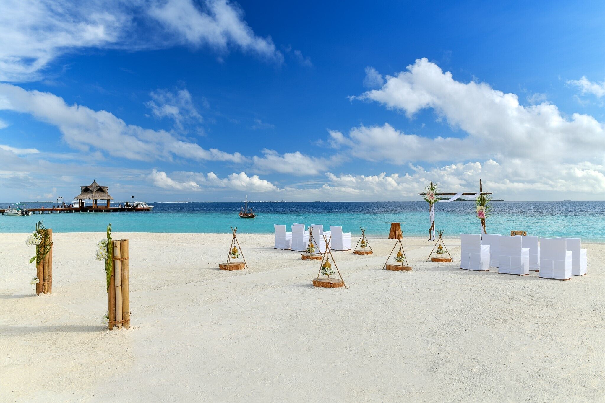 A beach wedding setup with white chairs and bamboo decorations.
