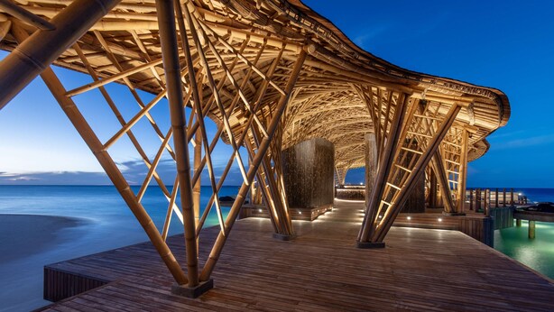 Una terrazza in legno con struttura in bambù sopra, che conduce a una zona piscina.