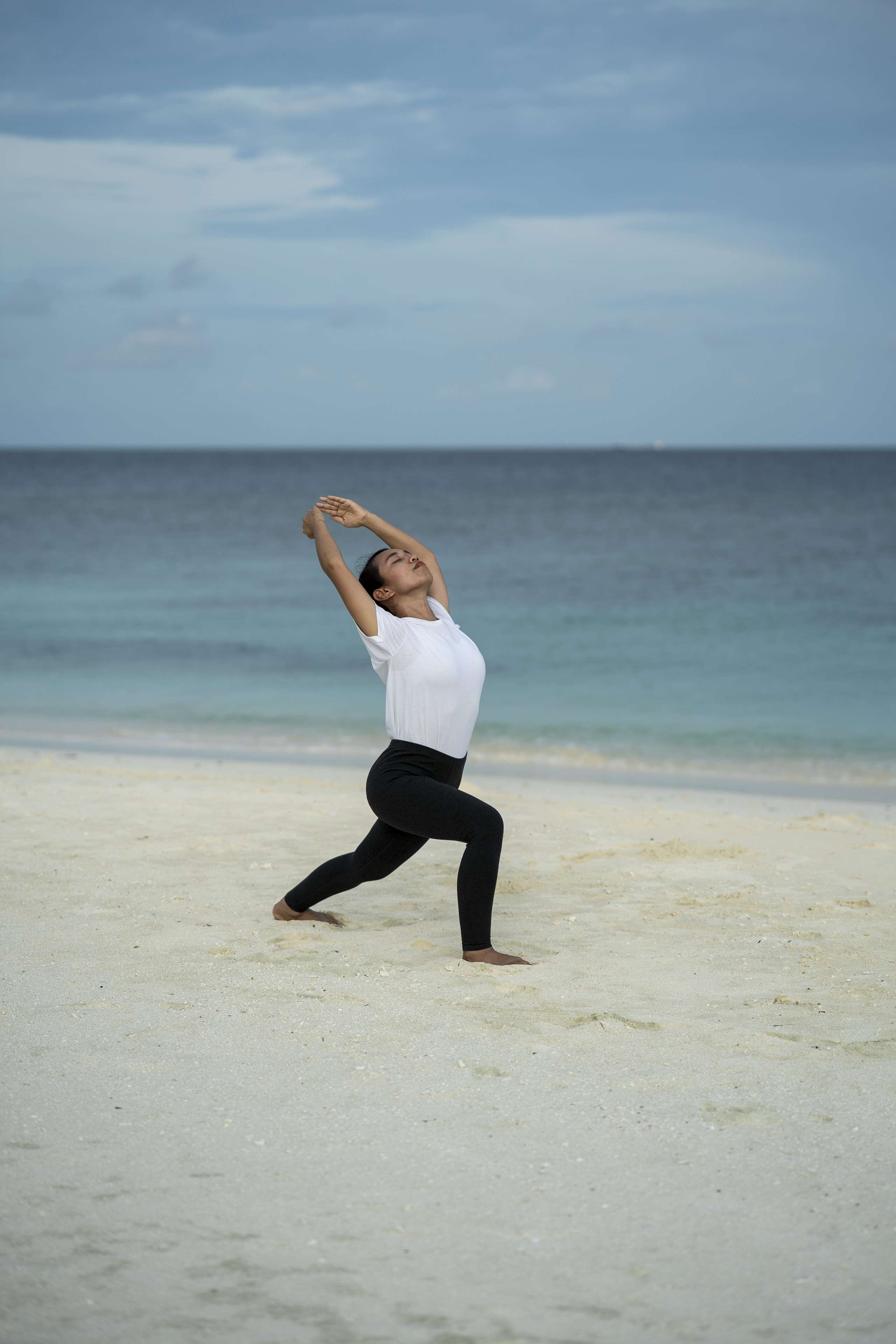 Una persona realizando una postura de yoga en una playa, con el océano al fondo.