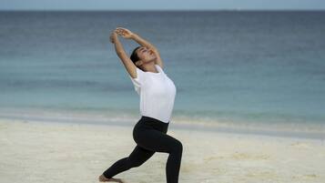 Una persona realizando una postura de yoga en una playa, con el océano al fondo.