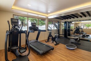 A modern gym with cardio equipment, a mirror, and large windows offering a view of the outdoors.