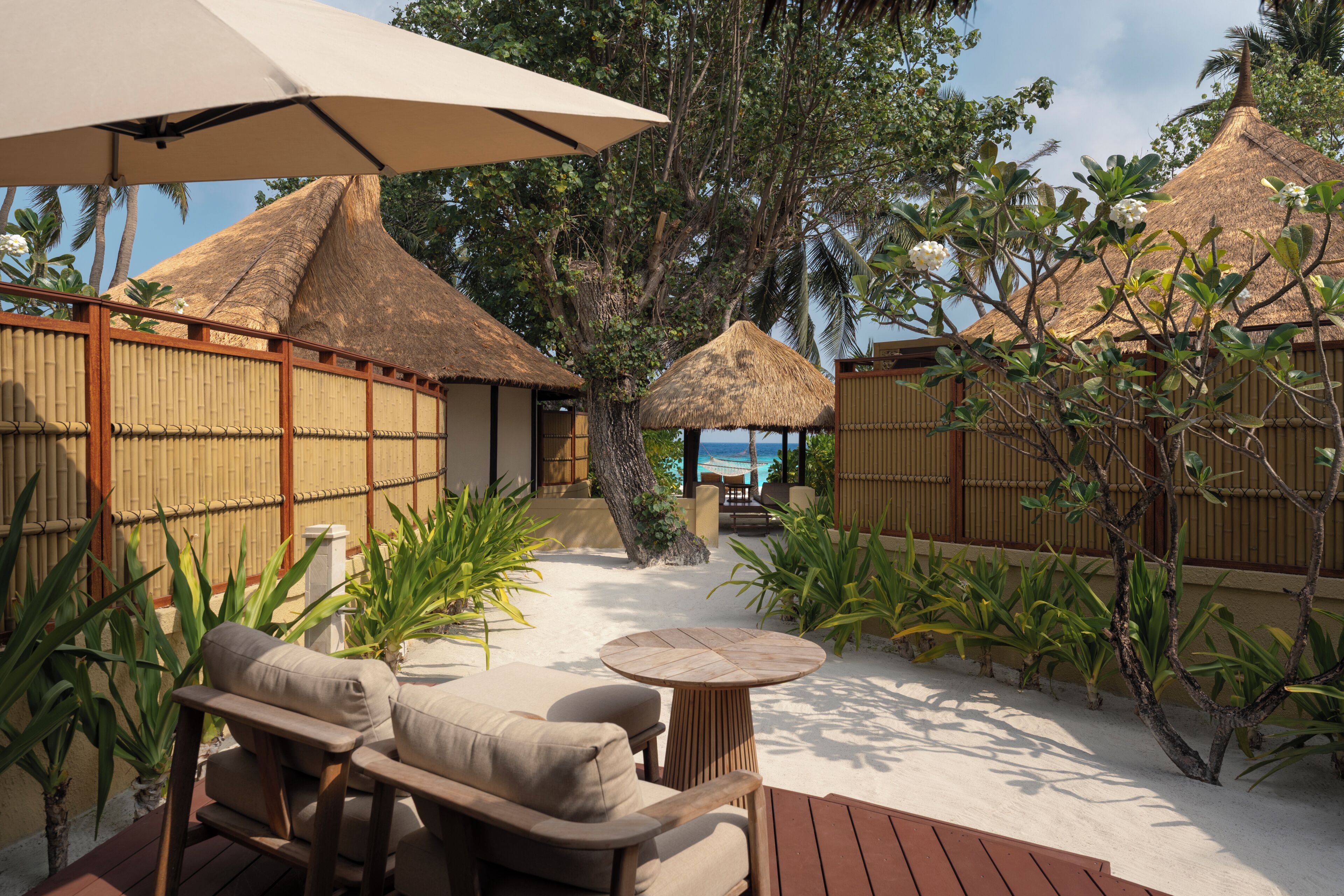 A tropical outdoor area with thatched-roof structures, a wooden deck, and lounge chairs.