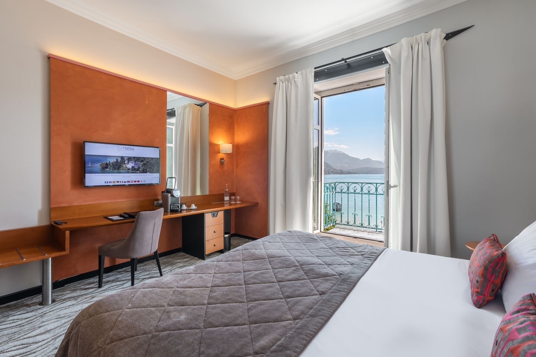 Une chambre d’hôtel équipée d’un lit, d’un bureau, d’une chaise, d’une télévision et d’un balcon avec vue sur la mer.