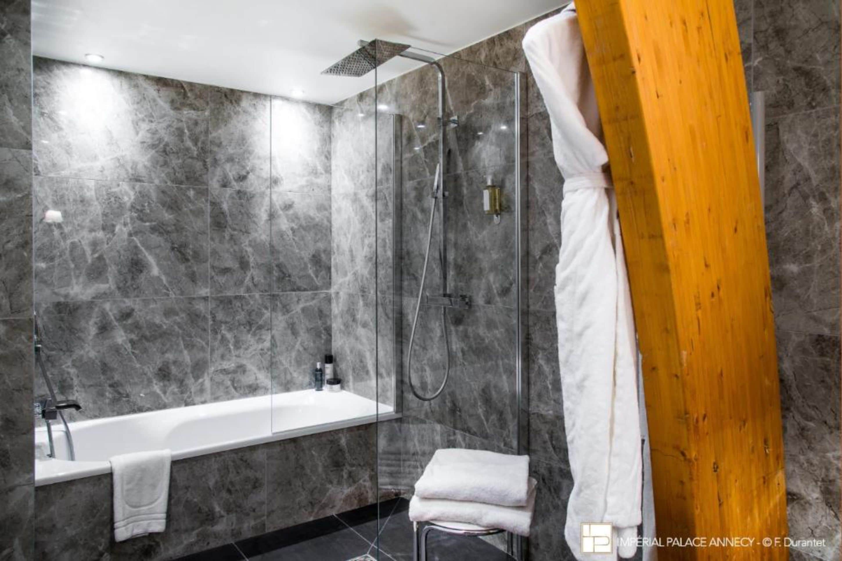 Ein modernes Badezimmer mit einer gläsernen Dusche, einer weißen Badewanne und einer Holzbank.