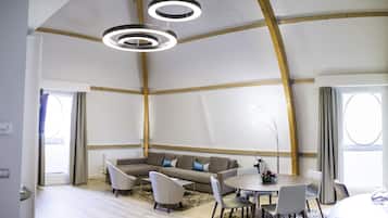 Une pièce spacieuse avec un plafond haut, des poutres en bois, un canapé d’angle, une table de salle à manger ronde avec des chaises et des luminaires suspendus.
