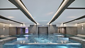 Una piscina interior moderna con una barrera de cristal, rodeada de zonas de estar y un diseño minimalista.