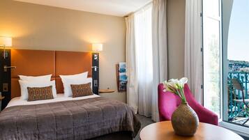 A hotel room with a bed, a nightstand, a vase with flowers, and a view of the outside balcony.