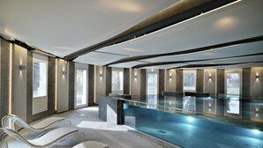 Una piscina interior moderna con sillas de descanso, ventanas amplias y un diseño elegante.