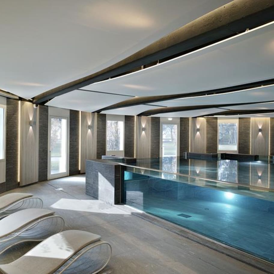 A modern indoor swimming pool with lounge chairs, large windows, and a sleek design.