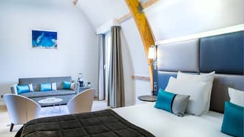 Une chambre d’hôtel moderne, dotée d’un grand lit, d’un canapé, d’une petite table et offrant une vue sur l’océan.