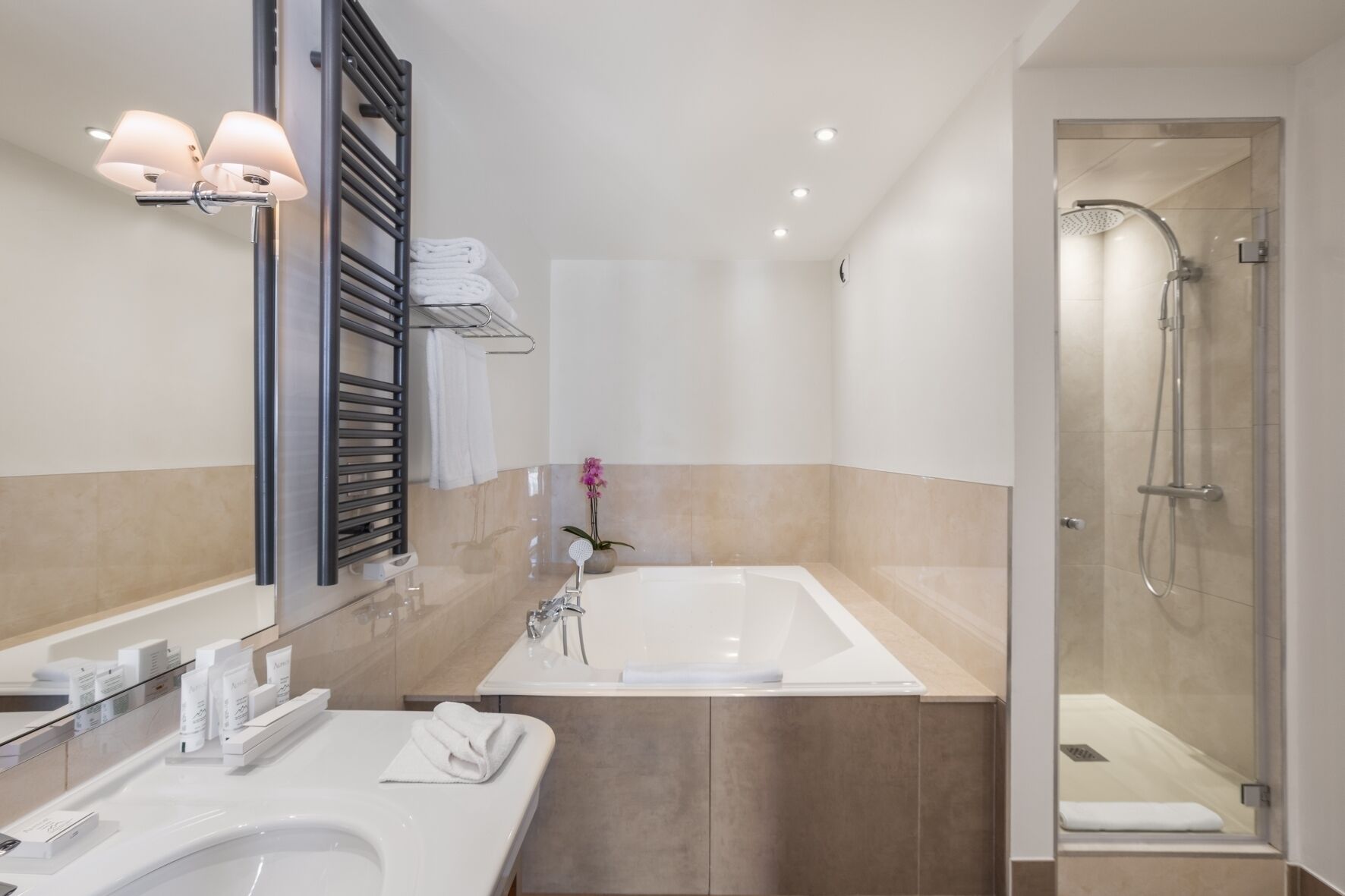 A modern bathroom with a large bathtub, a glass-enclosed shower, and a vanity with a mirror and towel rack.