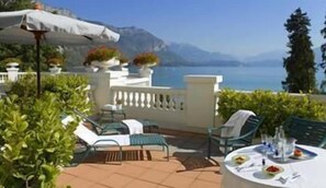 Une terrasse avec des sièges extérieurs, une table dressée pour le repas et une vue sur un lac et des montagnes.