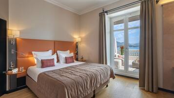 A hotel room with a large bed, a nightstand, a lamp, and a view of the outdoors.