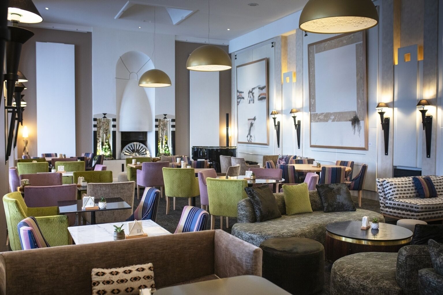 Een modern restaurant met kleurrijke stoelen en tafels, grote hanglampen en kunstwerken aan de muur.