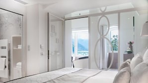 Una habitación de hotel moderna con una cama grande, un baño con cabina de ducha de vidrio y un balcón con vistas a la montaña.