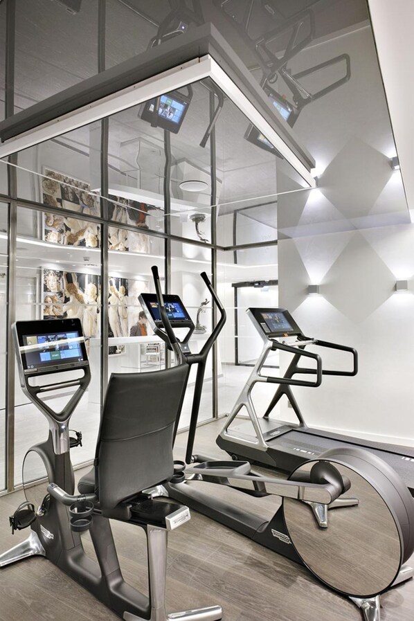 A modern gym with stationary bikes and treadmills, glass walls, and a digital display.