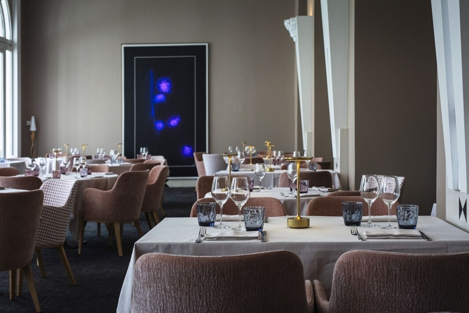 A restaurant with tables set for dining, chairs, and a large screen in the background.