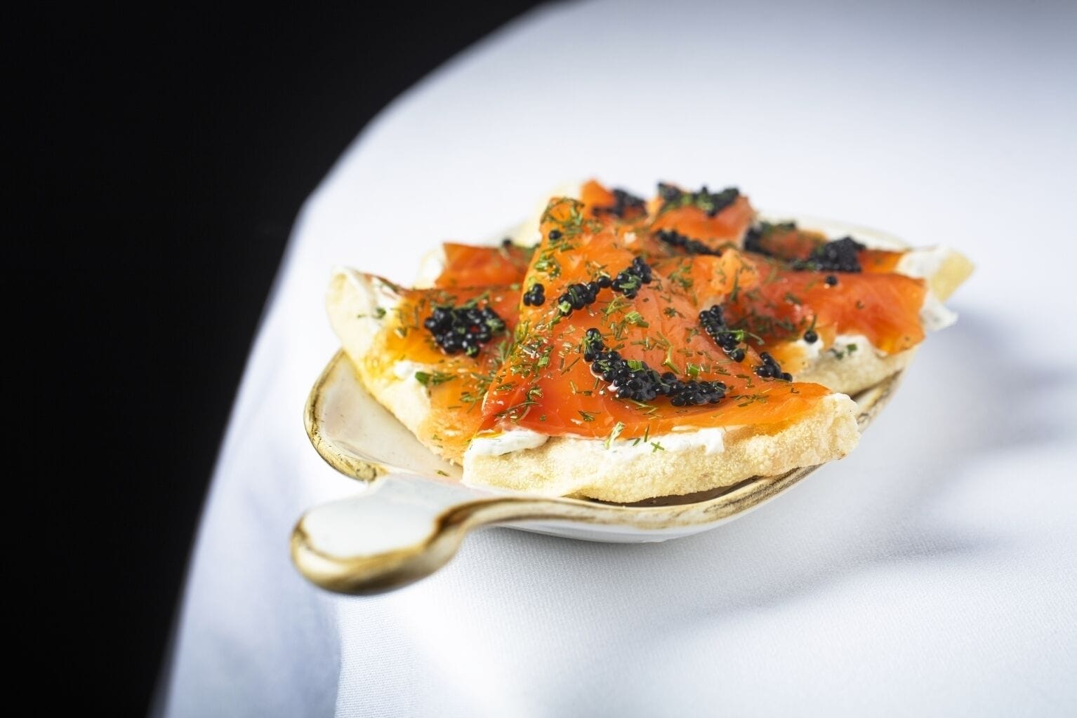A single slice of bread topped with smoked salmon, black caviar, and herbs.