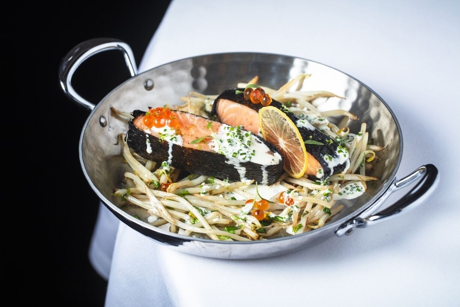 A stainless steel bowl containing a seafood dish with salmon, lemon slices, and garnishes.