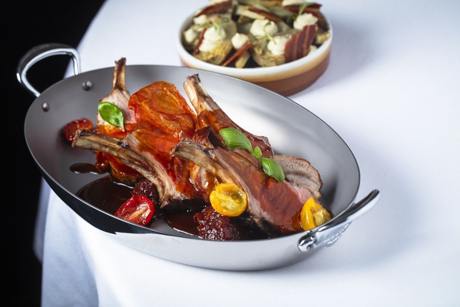 A pan with roasted lamb chops garnished with herbs and vegetables.