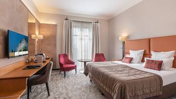Een hotelkamer met een bed, twee stoelen, een bureau, een televisie en een raam met gordijnen.