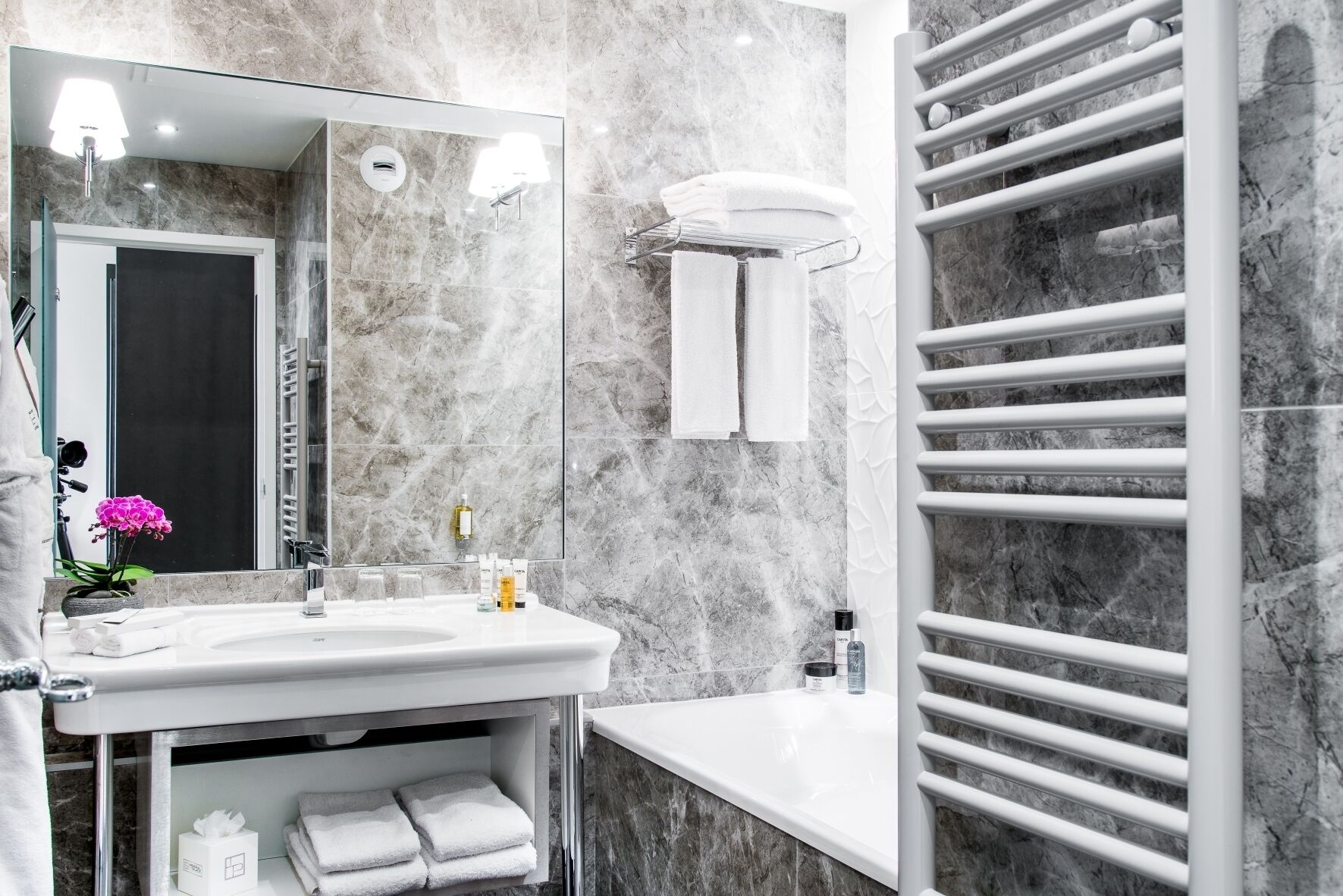 A modern bathroom with a marble backsplash, a large mirror, a white sink, and a towel rack.
