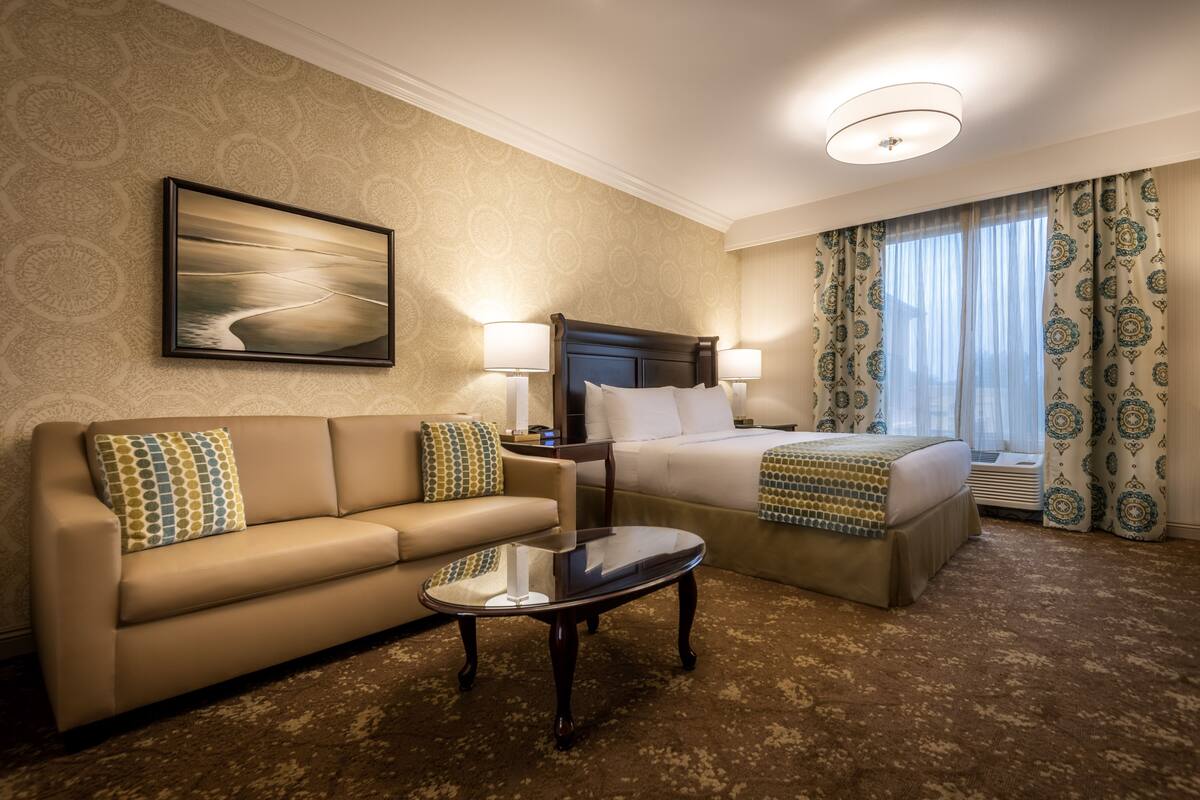 A hotel room with a bed, a sofa, a coffee table, and a painting on the wall.