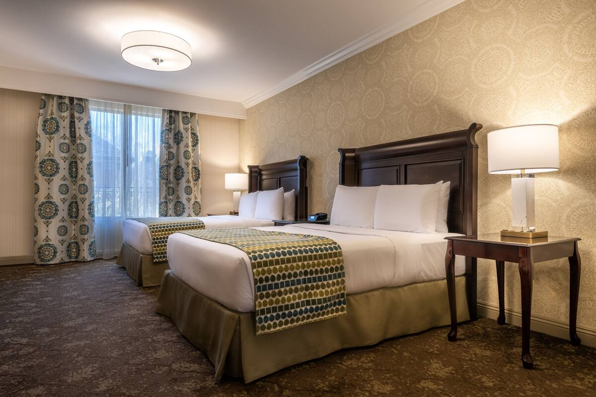 A hotel room with two beds, a nightstand, a lamp, and a patterned carpet.