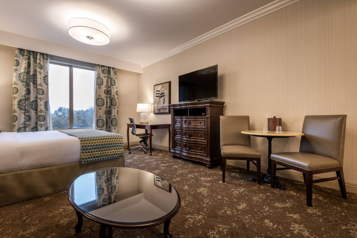 A hotel room with a bed, a desk, a television, and two chairs.