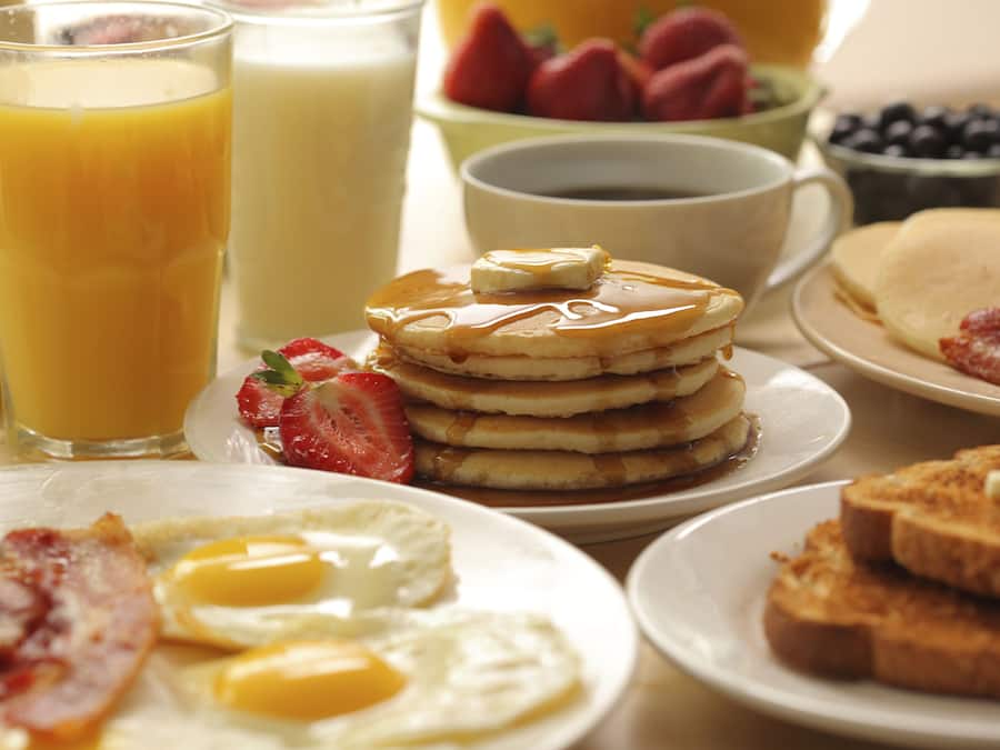 A breakfast setting with pancakes, eggs, bacon, and fruit.