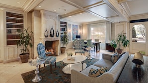A spacious living room with a fireplace, comfortable seating, a coffee table, and a bookshelf filled with books. - Ayres Hotel Seal Beach - Cypress (Seal Beach)