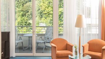 Una habitación con dos sillones naranja, una mesa de vidrio, una lámpara y vistas a un balcón con una silla y una mesa.