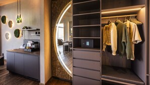 Habitación de hotel moderna con armario empotrado, escritorio con cafetera y espejo circular.