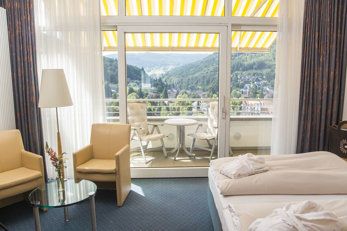 A hotel room with a balcony, a bed, two chairs, a small table, and a lamp.