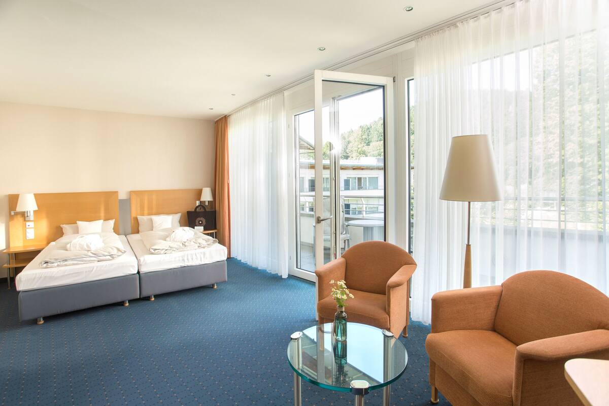 A hotel room with two beds, a glass coffee table, a sofa, and a view through the window.